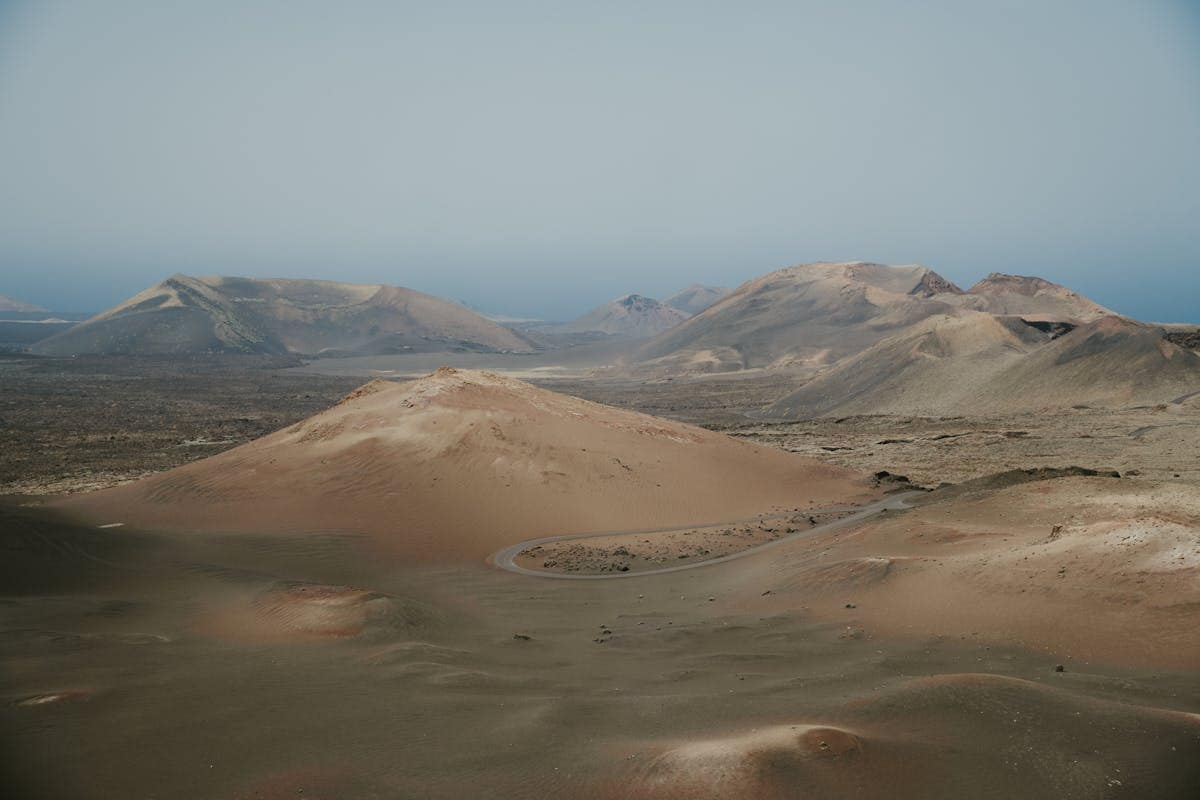 Aerial view of volcanic craters and barren lava terrain in Lanzarote, Canary Islands, with the Atlantic Ocean visible in the distance