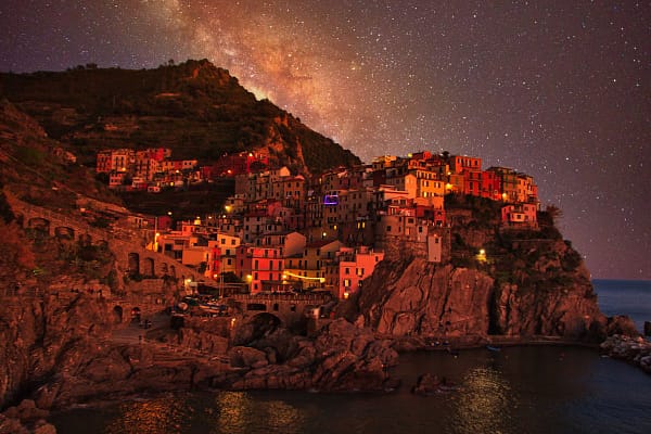 Manarola village lights reflected in the harbour water at night, Cinque Terre