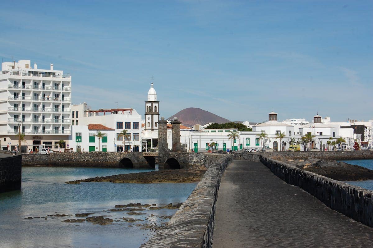 Stone causeway leading to Arrecife old town with white buildings, a church tower and a volcanic mountain visible behind