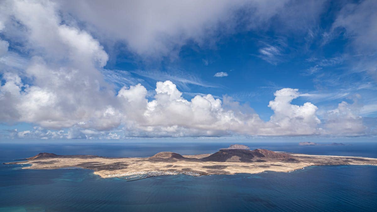 Aerial view of La Graciosa island from Mirador del Río on Lanzarote, showing turquoise Atlantic waters and a dramatic blue sky with clouds