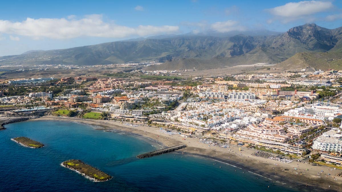 Aerial view of a Tenerife coastal resort town with mountains in the background