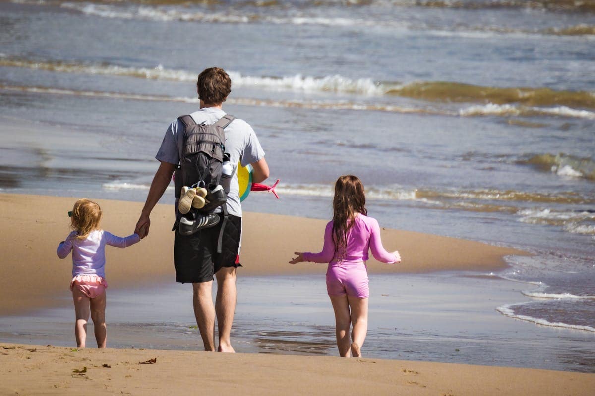 A father and his two young children walking along the beach at the water's edge on a summer family holiday
