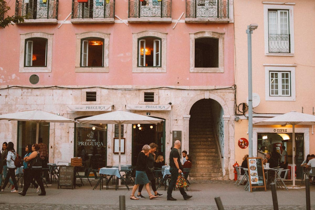 Outdoor cafe tables on a sunlit Lisbon street, with locals and visitors eating and drinking