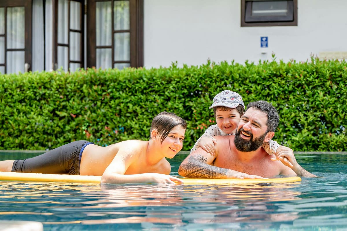 A father and children laughing on a pool float at a sunny holiday resort