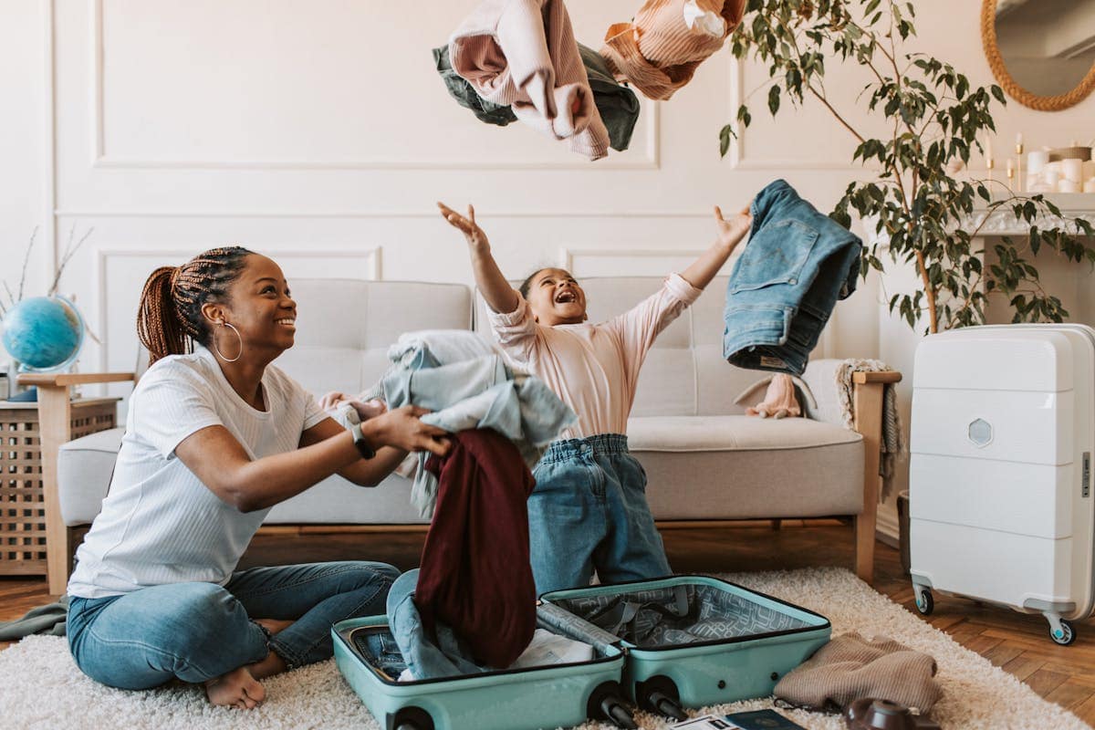 Mother and daughter joyfully packing clothes into a suitcase before a holiday