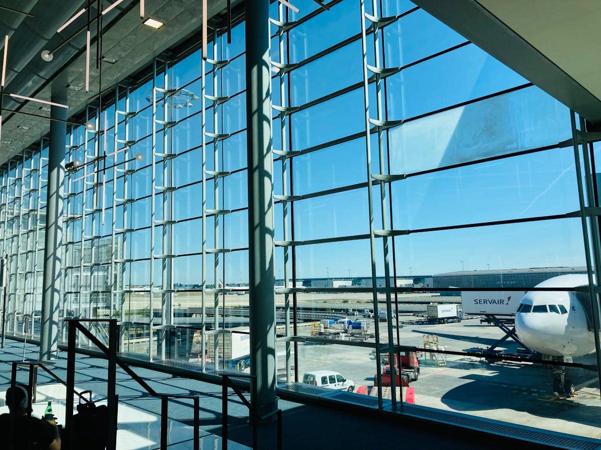 A modern airport departure lounge with a large glass facade overlooking a passenger aircraft on the tarmac