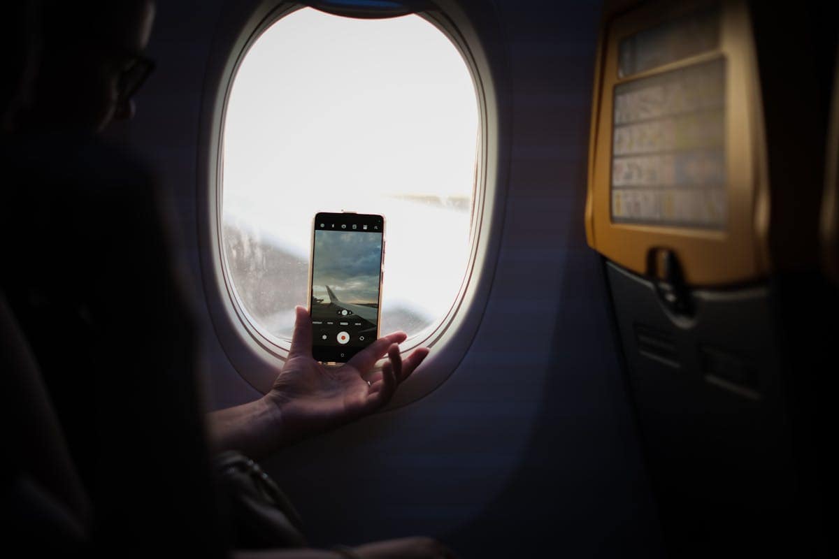 Passenger looking out of plane window, photographing the aircraft wing in flight
