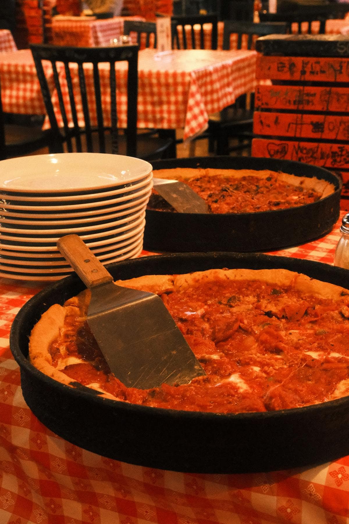 Deep dish pizza slice being lifted from a pan, showing layers of cheese and tomato sauce