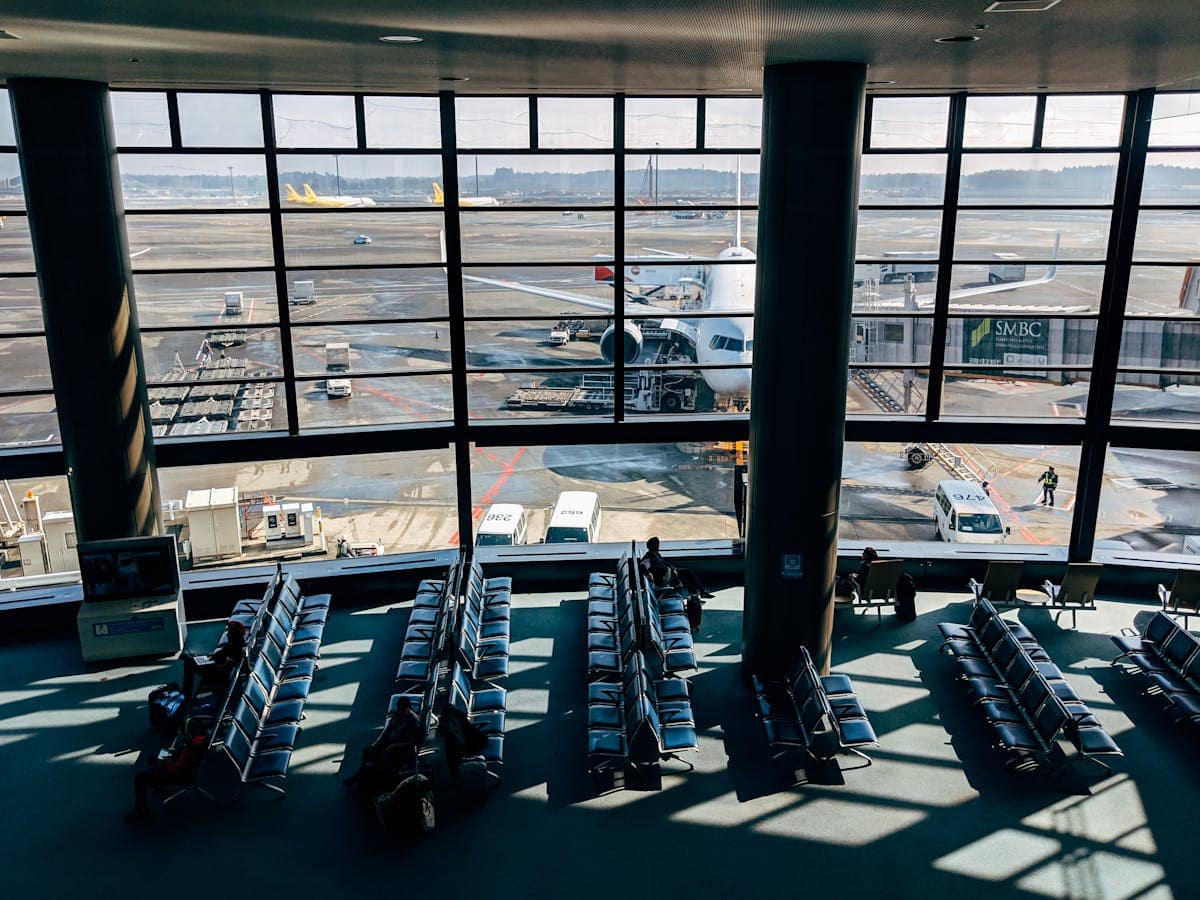 Travellers walking through a bright modern airport corridor with glass walls, suitcases in hand