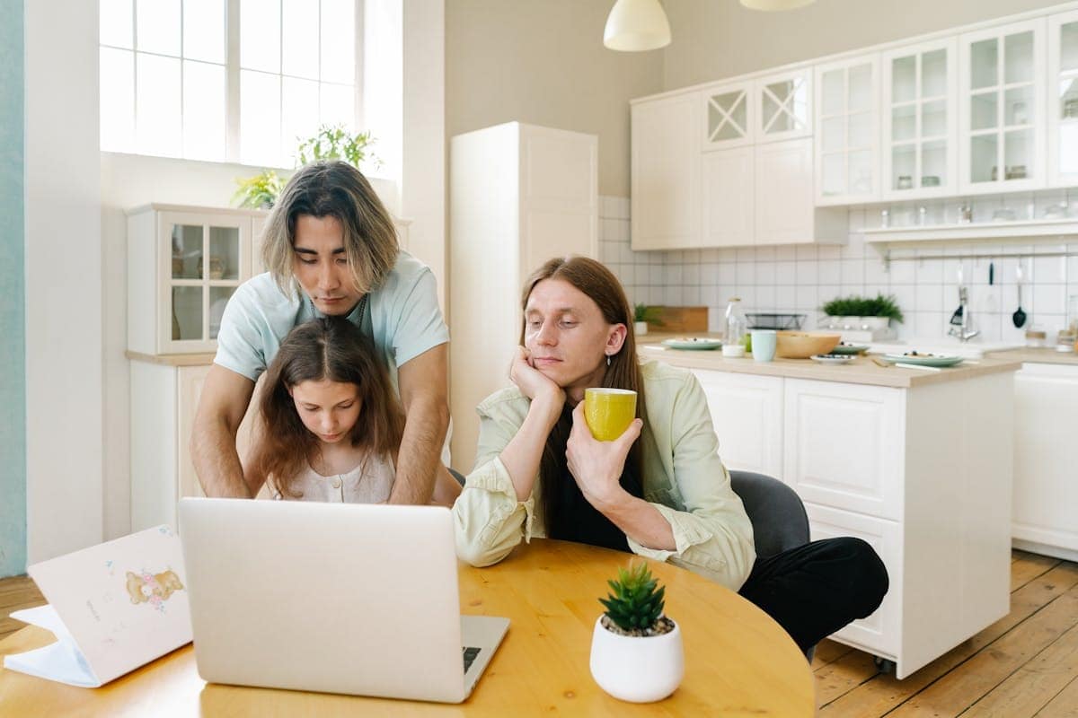Family planning a school holiday trip online Family gathered around a laptop in a kitchen, planning a school holiday trip